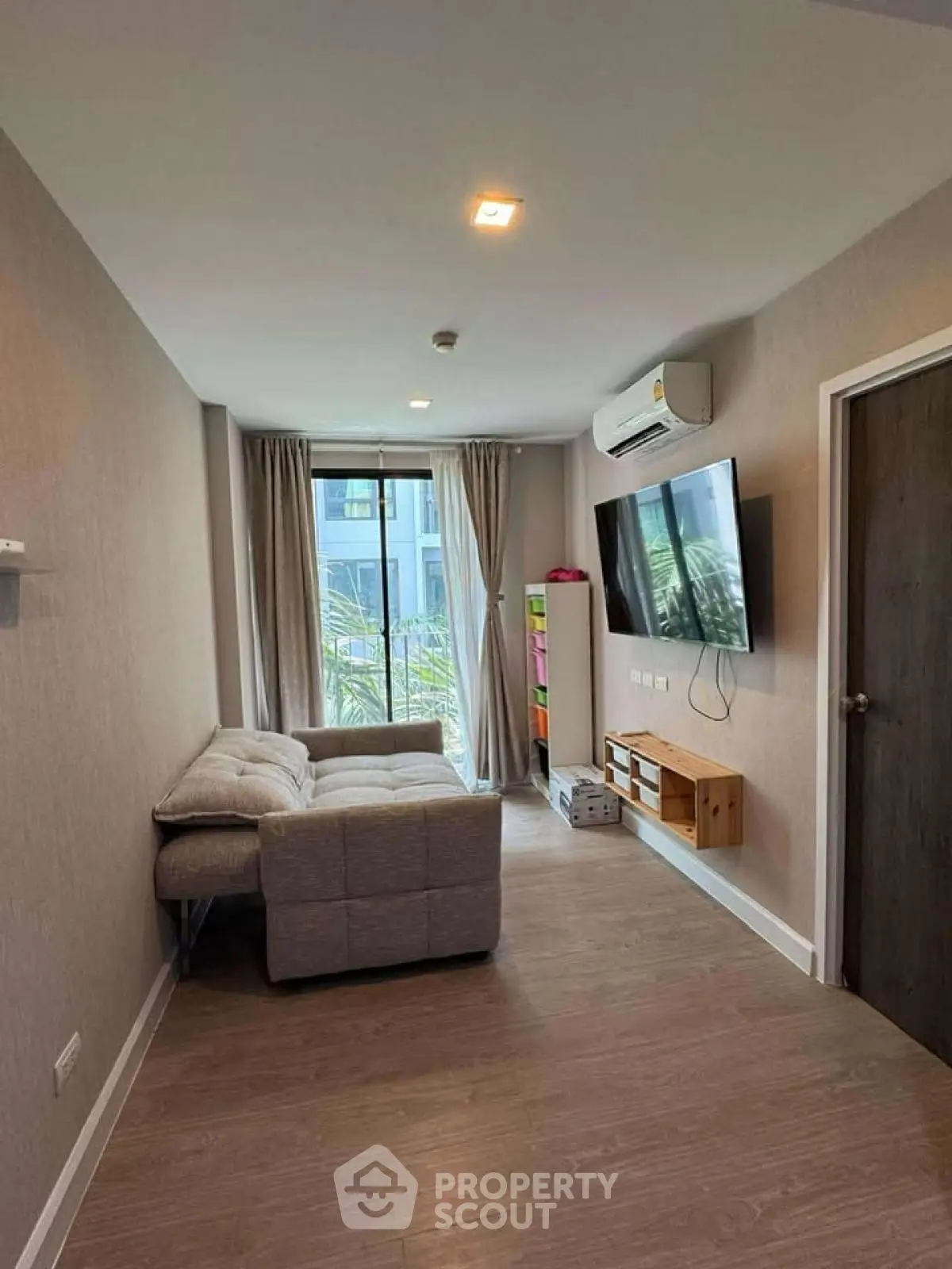 Modern living room with cozy sofa, wall-mounted TV, and large window for natural light.