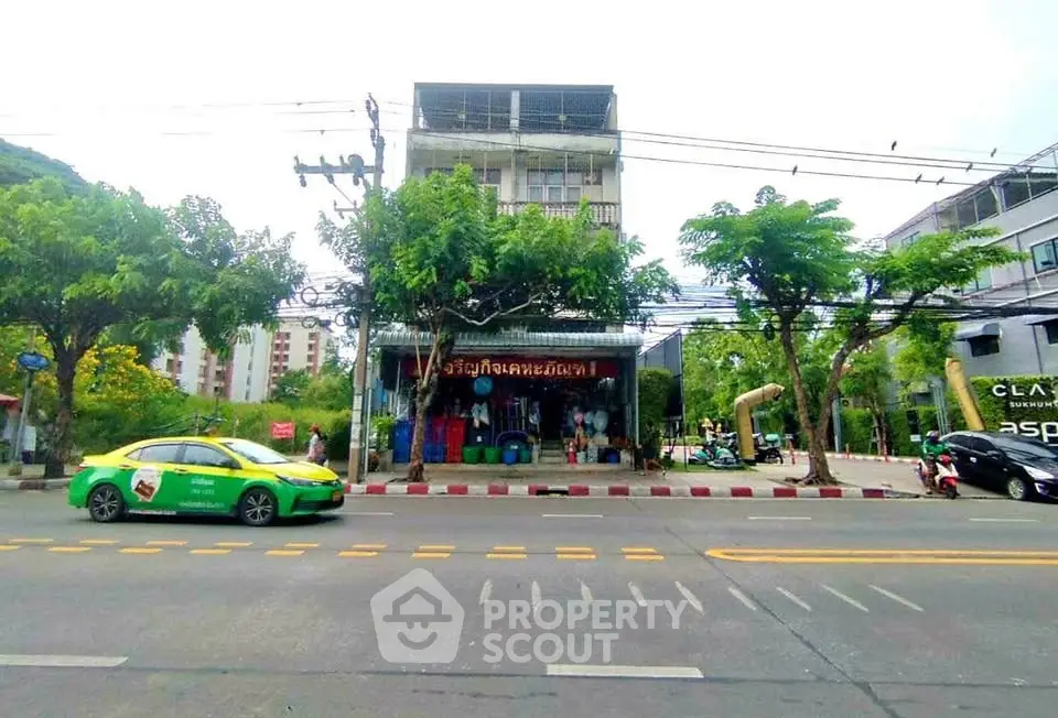 Street view of a commercial building with trees and parked vehicles in urban setting.