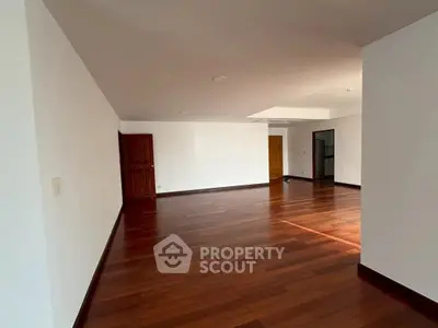 Spacious empty living room with wooden flooring and white walls, ideal for customization.