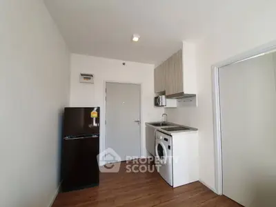 Compact kitchen with modern appliances, featuring a fridge and washing machine, in a cozy apartment setting.