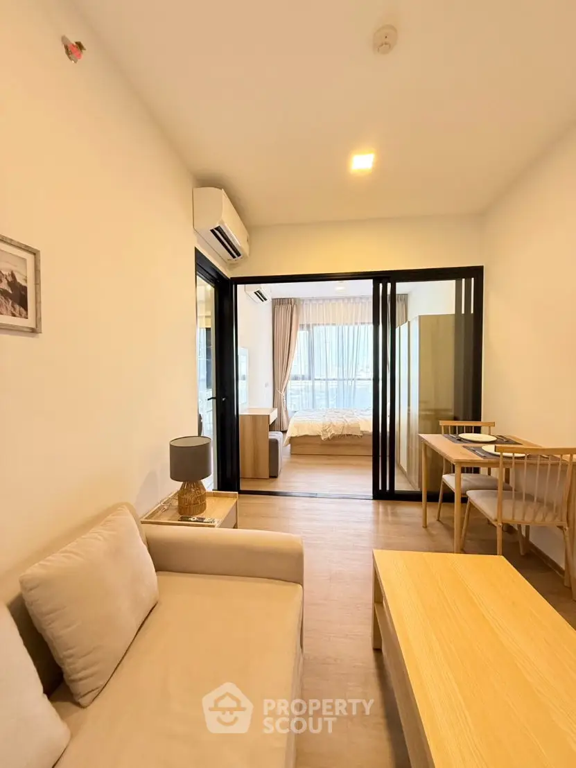 Modern living room with cozy seating and view into a stylish bedroom through sliding glass doors.