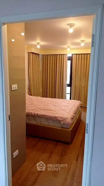Cozy bedroom with wooden flooring and soft lighting, featuring a comfortable bed and elegant curtains.