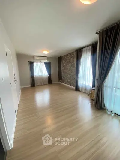 Spacious empty living room with wooden flooring and large windows with curtains.