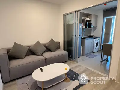 Modern living room with cozy sofa and adjacent kitchen featuring washing machine and microwave.