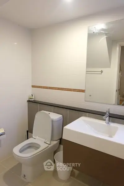 Modern bathroom with sleek fixtures and neutral tones, featuring a large mirror and contemporary sink.