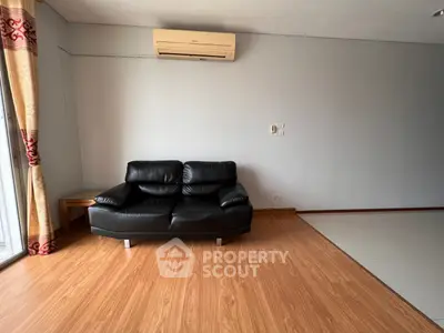 Spacious living room with modern black leather sofa and air conditioning, featuring elegant wooden flooring.