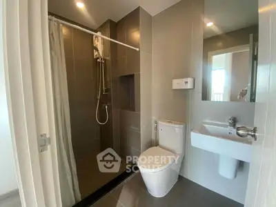 Modern bathroom with sleek design featuring shower, toilet, and sink in a contemporary apartment.
