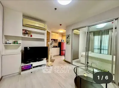 Modern living room with open kitchen and bedroom view, featuring sleek furniture and bright lighting.