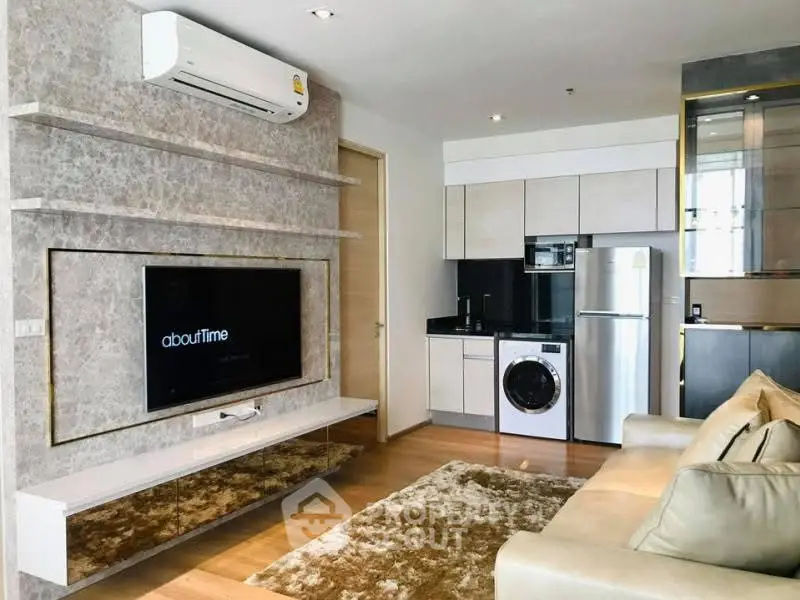 Modern living room with integrated kitchen, featuring a washing machine and sleek appliances.