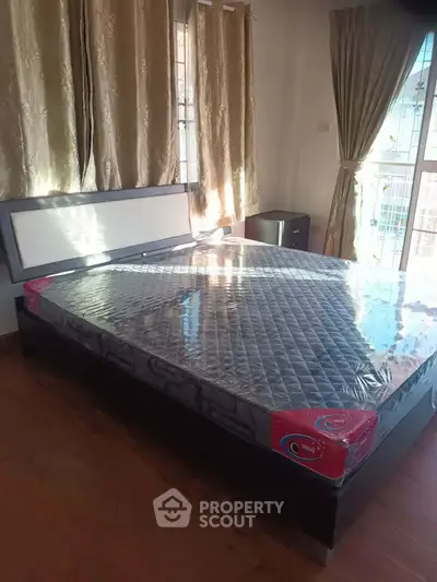 Spacious bedroom with large windows and elegant curtains, featuring a new mattress on a stylish bed frame.