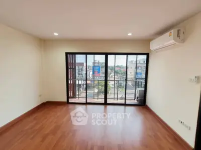 Spacious living room with wooden flooring and large windows offering city views.