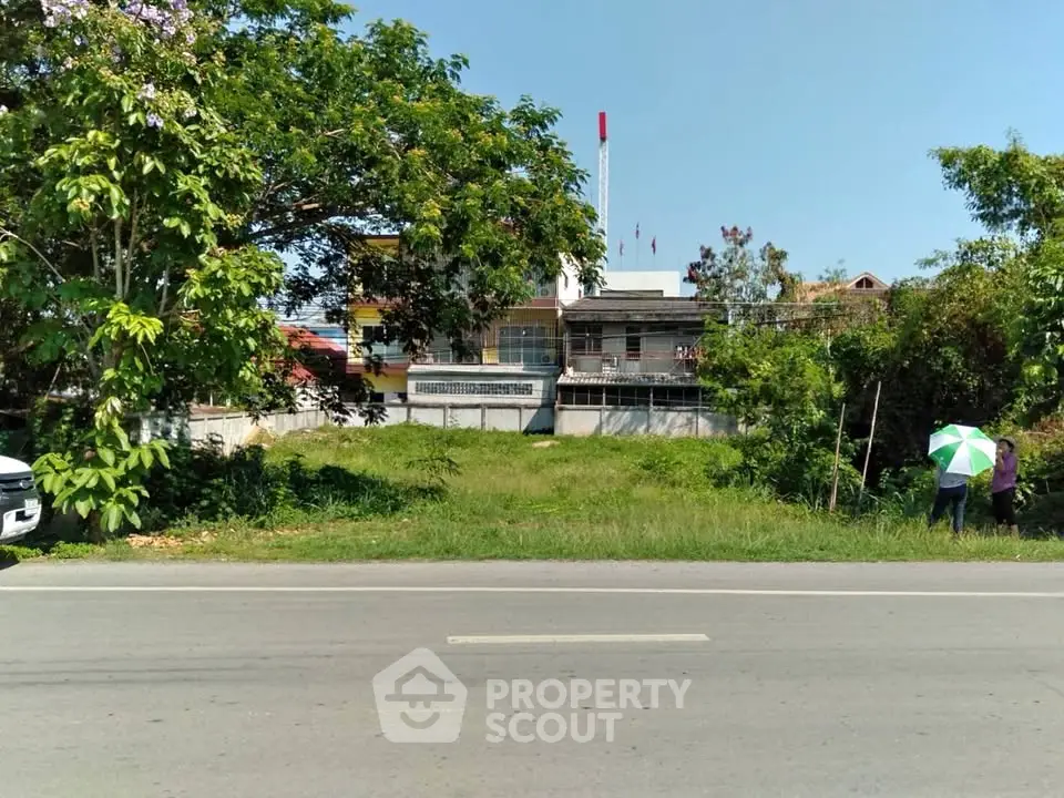 Vacant land plot with lush greenery and potential for development, located near a main road.