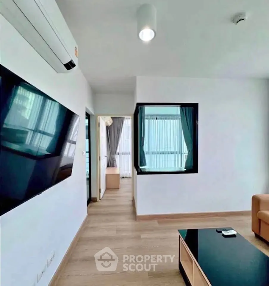 Modern living room with sleek TV and air conditioning, featuring a cozy seating area and wooden flooring.