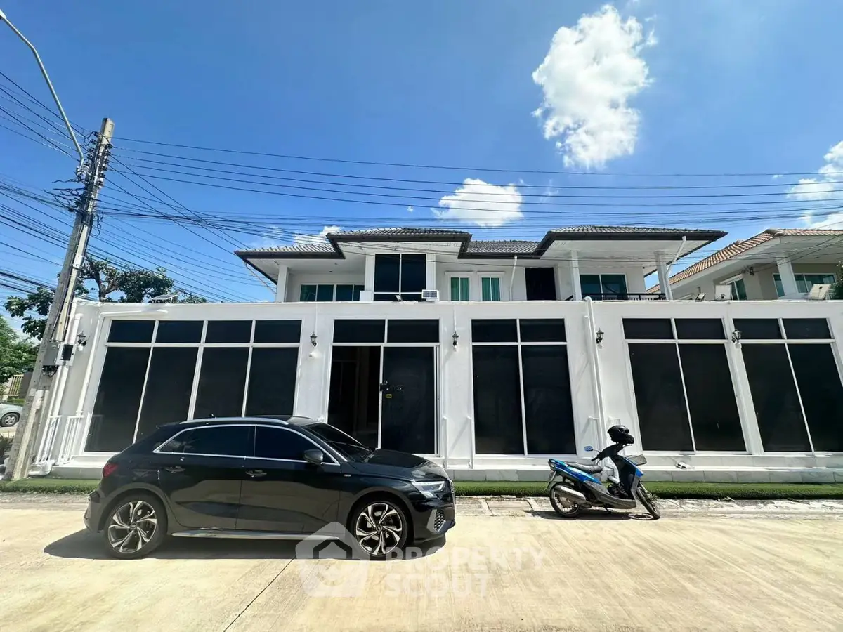 Modern two-story house with large windows and sleek design, featuring a car and motorcycle parked outside.