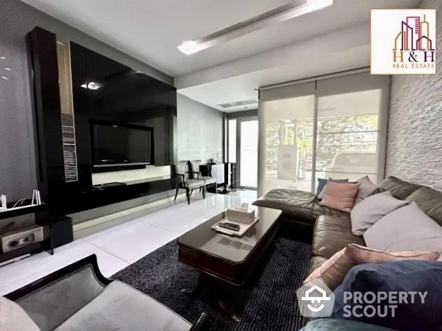 Luxurious living room with sleek modern design, featuring a large L-shaped sofa, dark rug, and a wall-mounted TV, opening to a bright dining area.