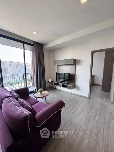 Modern living room with purple sofa and wall-mounted TV, featuring large windows and sleek flooring.