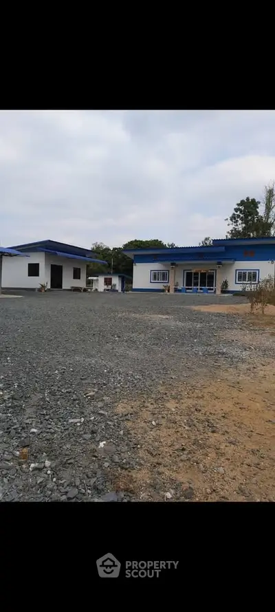 Charming rural property with blue-roofed buildings and spacious gravel driveway.