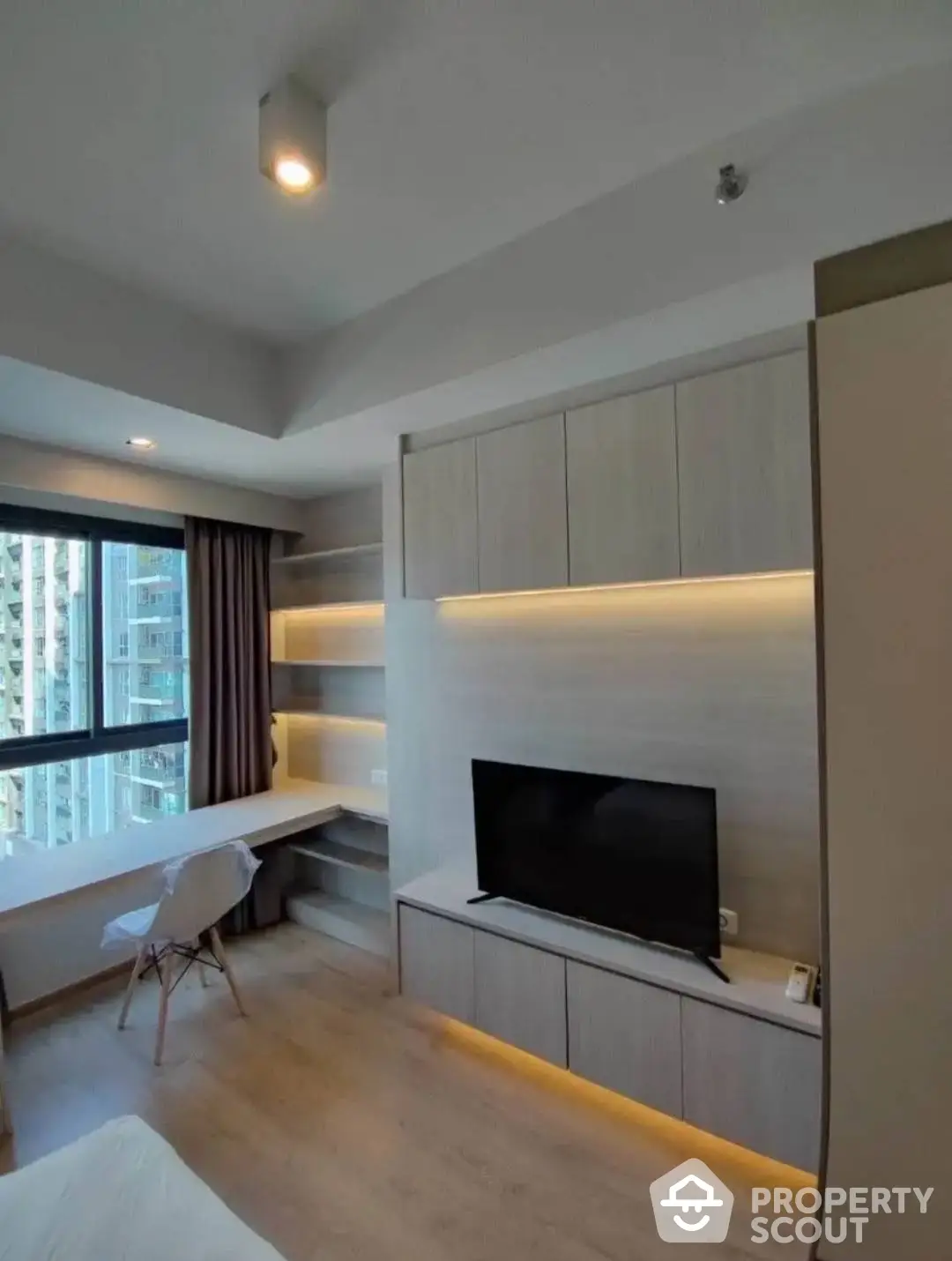 Modern living room with sleek built-in cabinetry and ambient lighting, complemented by a large window offering natural light.