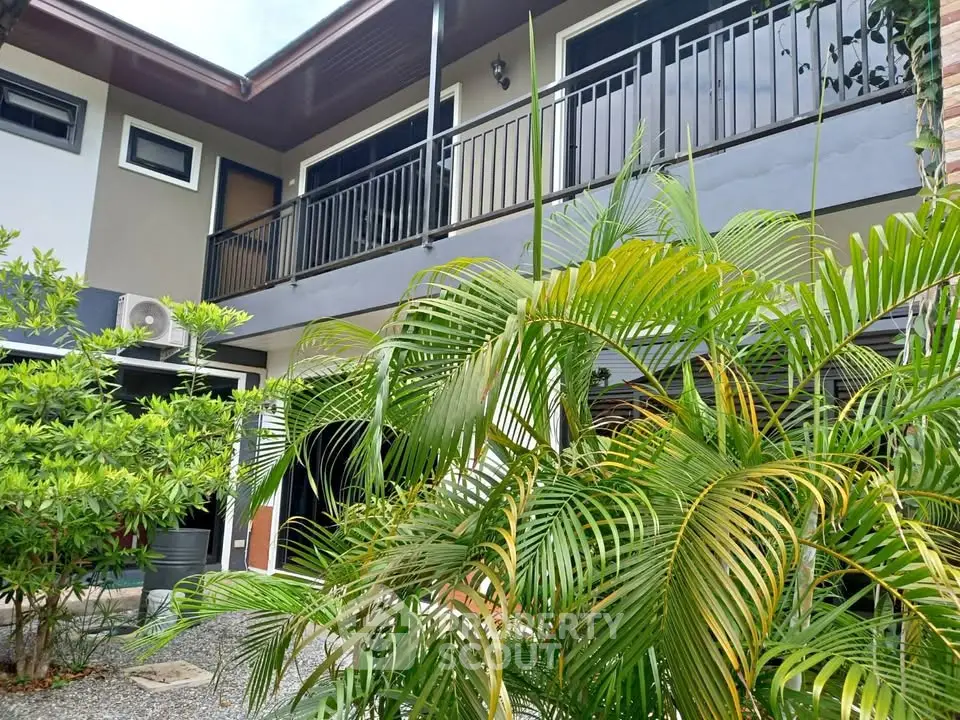 Modern two-story building with lush greenery and balcony, perfect for serene living.