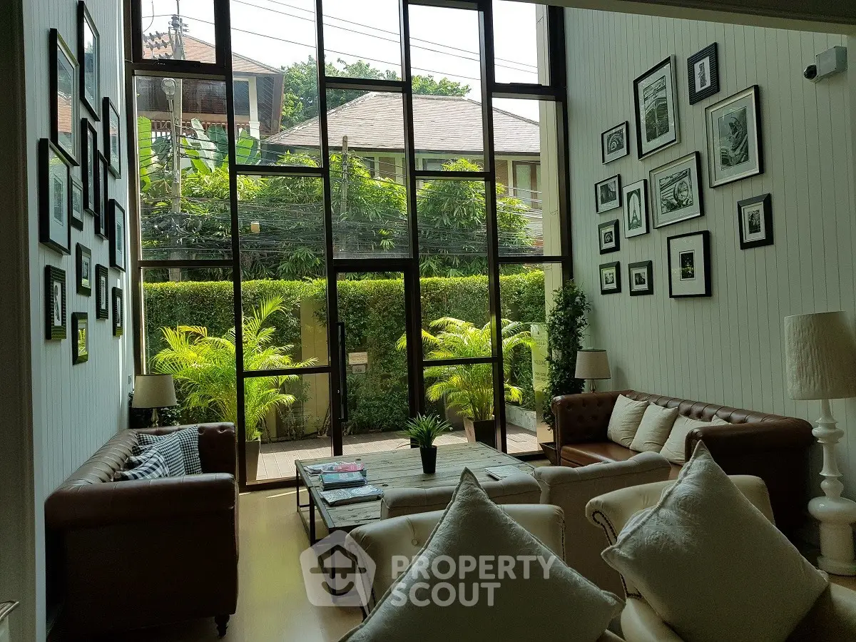 Spacious living room with high ceilings and large windows overlooking lush greenery, featuring elegant decor and cozy seating.