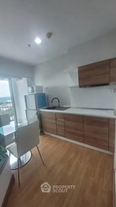 Modern kitchen with sleek cabinets and wooden flooring, featuring a compact dining area and large window view.