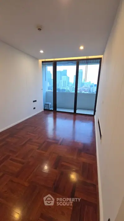 Spacious room with wooden flooring and stunning city view through large windows.