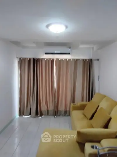 Cozy living room with yellow sofa and curtains, featuring air conditioning.
