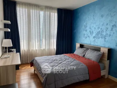 Modern bedroom with blue accent wall and large window, featuring a cozy bed and stylish desk.