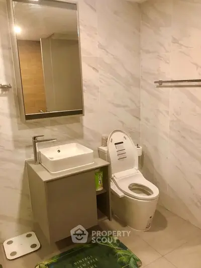 Modern bathroom with sleek fixtures and elegant marble walls, featuring a stylish vanity and contemporary toilet.