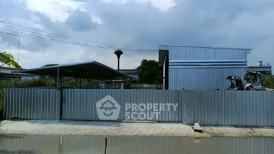 Industrial property with metal fencing and warehouse structure under cloudy sky.