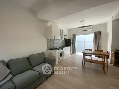 Modern living room with open kitchen and dining area, featuring a washing machine and stylish decor.