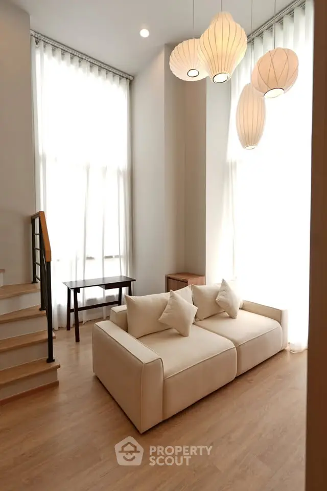 Elegant living room with high ceilings, modern lighting, and cozy seating in a bright, airy space.