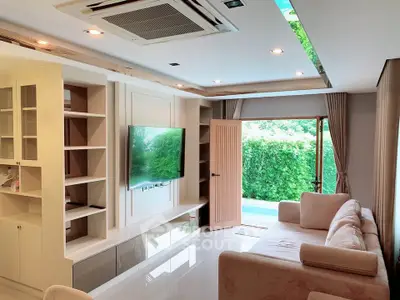 Spacious living room with modern decor and garden view, featuring built-in shelves and a wall-mounted TV.