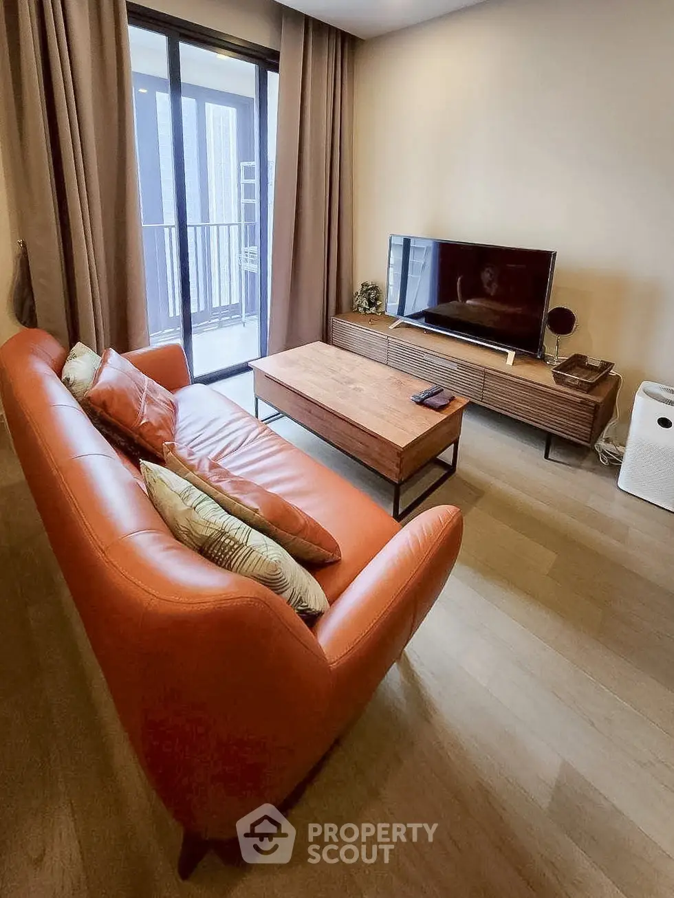 Modern living room with stylish orange sofa and sleek TV setup, featuring a cozy balcony view.