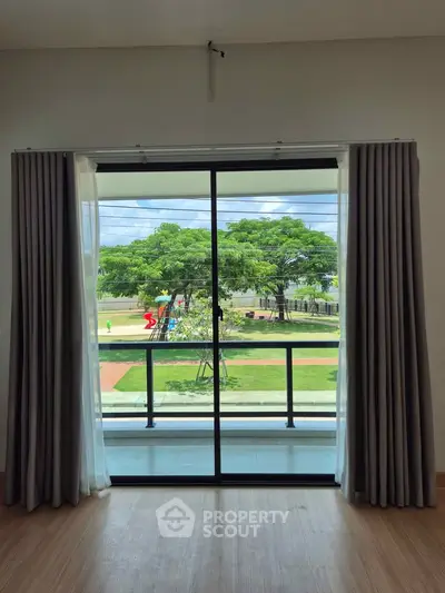 Spacious room with large sliding glass doors opening to a balcony with a scenic view of a park.