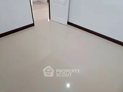 Spacious empty room with glossy tiled flooring and open door, ideal for customization.