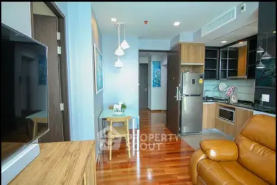 Modern open-layout living room with sleek kitchen and cozy seating area, featuring hardwood floors and stylish lighting.