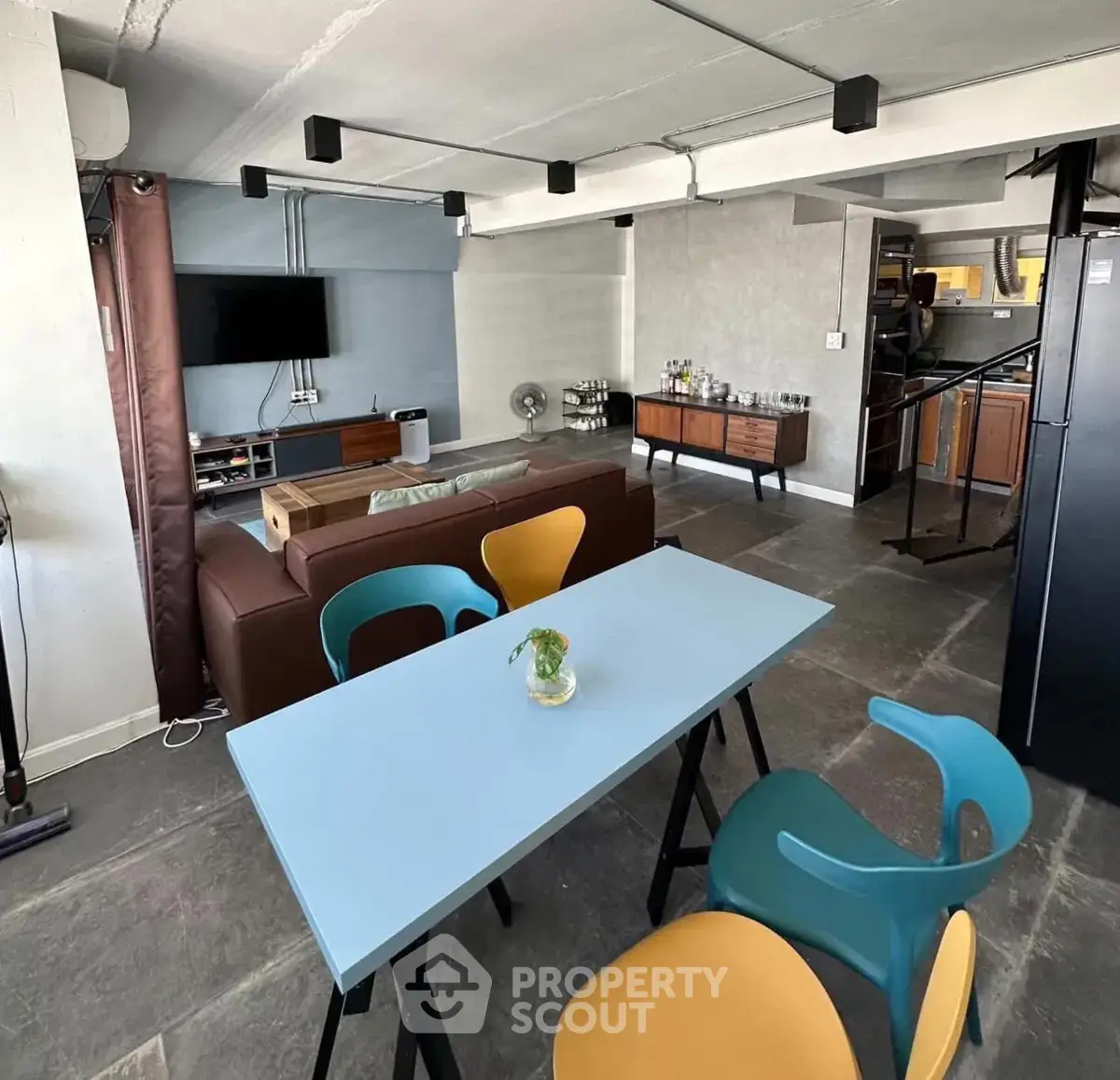 Modern industrial-style living room with colorful dining chairs and open kitchen layout.