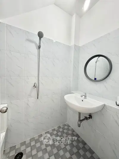 Modern bathroom with sleek white tiles and round mirror, featuring a minimalist shower and sink design.