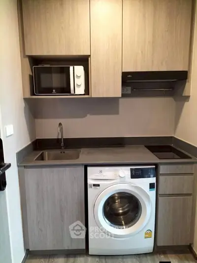 Modern compact kitchen with washing machine and microwave in sleek cabinetry.