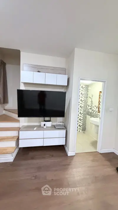 Modern living room with sleek TV setup and adjacent bathroom, featuring stylish wooden flooring and contemporary design.