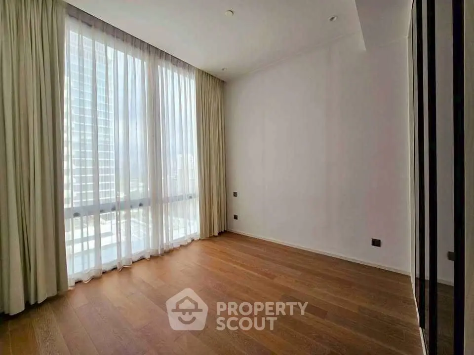 Spacious empty room with large window and wooden flooring in modern apartment.
