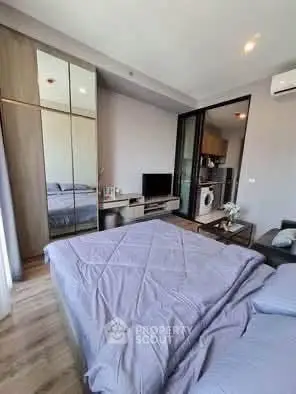 Modern bedroom with mirrored wardrobe and compact living area in stylish apartment.