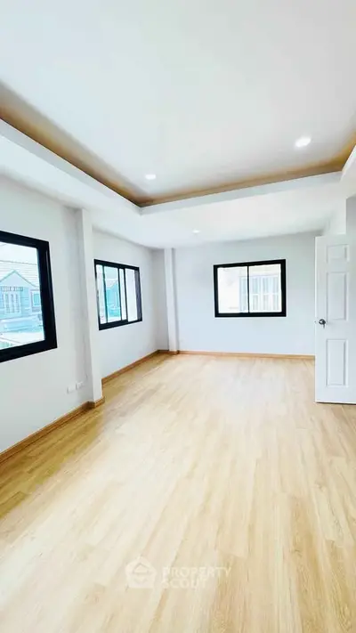 Spacious empty room with large windows and wooden flooring, perfect for customization.
