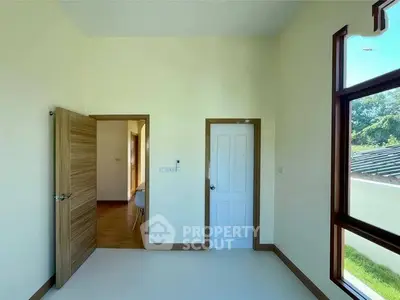 Bright empty room with large window and wooden doors, perfect for customization.