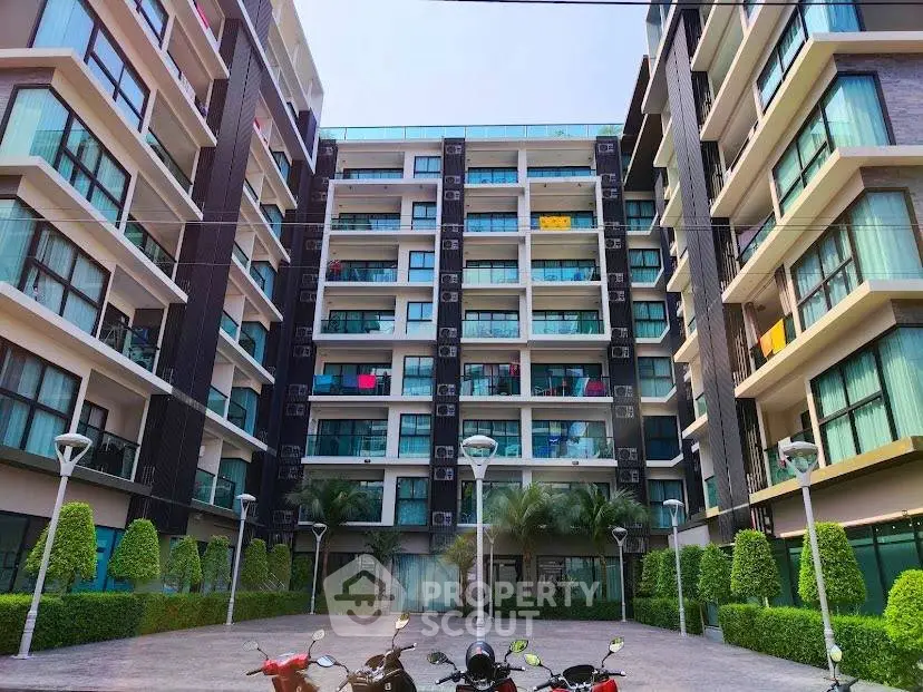 Modern apartment building exterior with lush greenery and parked motorcycles.