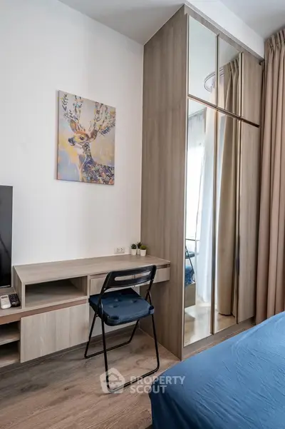 Modern bedroom with stylish decor and mirrored wardrobe, featuring a cozy workspace and elegant artwork.