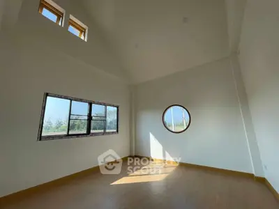 Spacious room with unique round window and high ceiling, perfect for natural light.