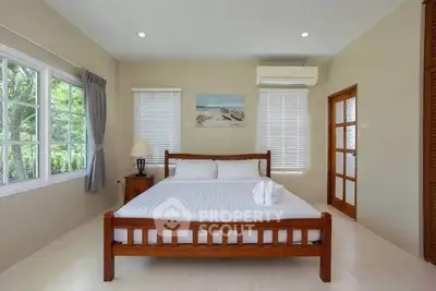 Spacious bedroom with large windows and elegant decor, featuring a comfortable wooden bed and serene ambiance.