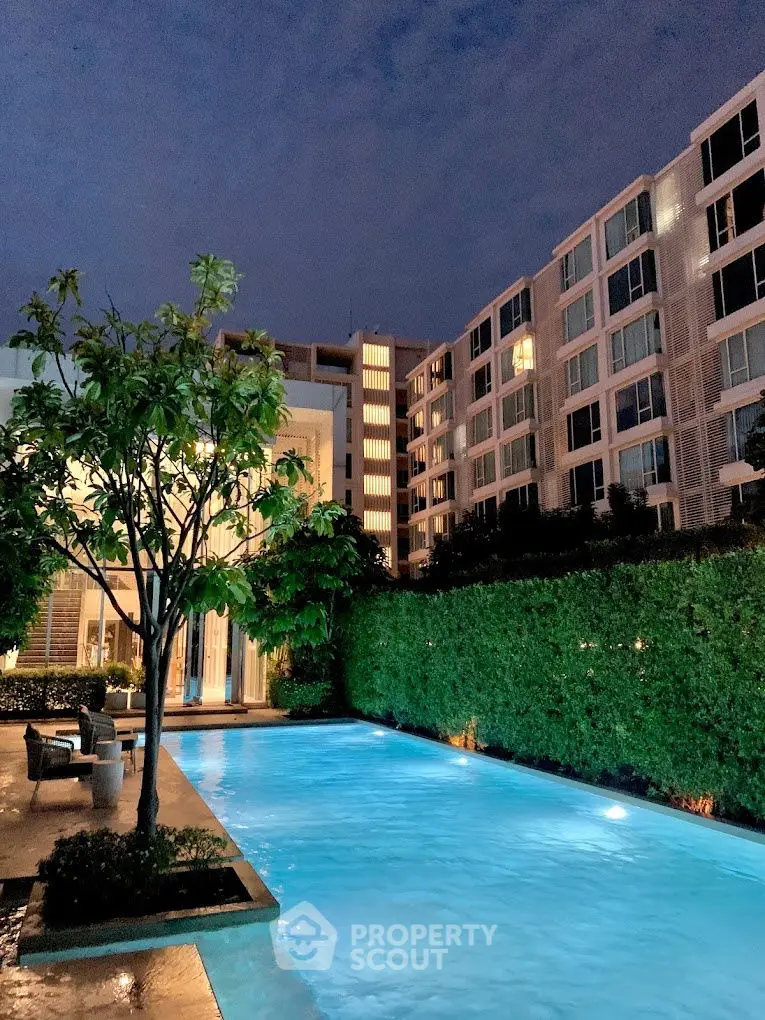 Luxurious apartment complex with illuminated pool and lush greenery at dusk.